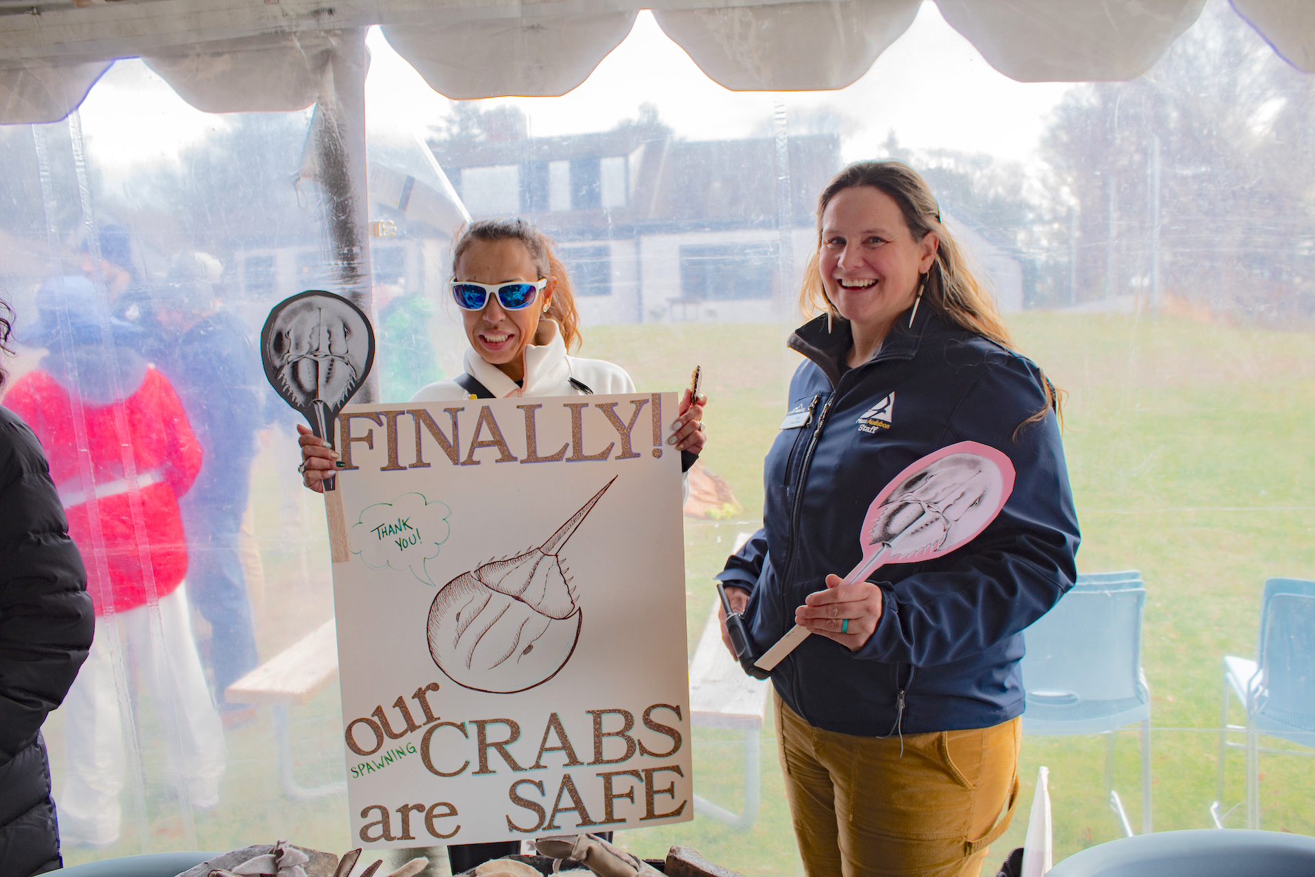 Two women stand, one holding a sign that says FINALLY! our CRABS are SAFE