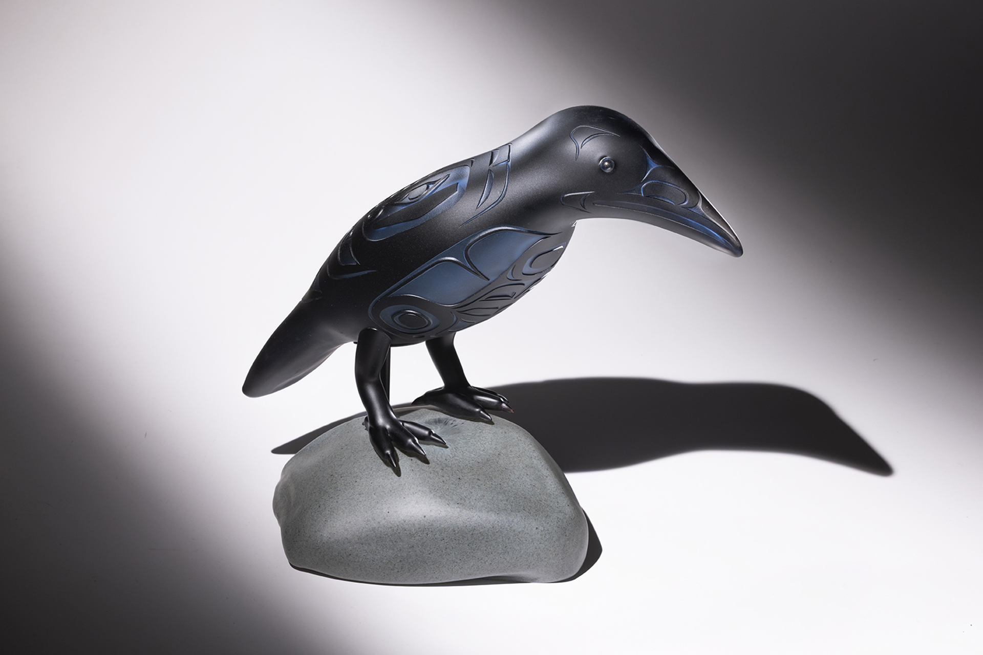 Glass sculpture of a raven perched on a rock.