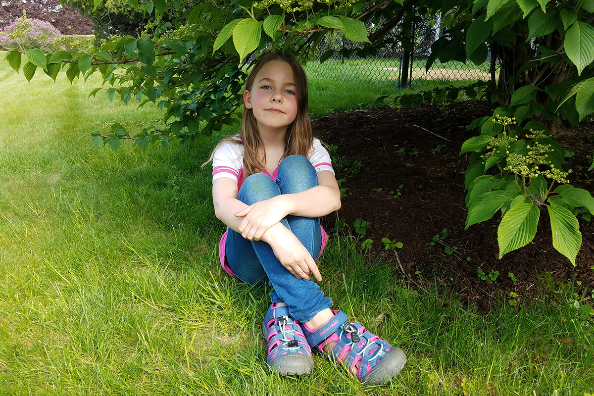 Young girl sitting in the grass, smiling at the camera.