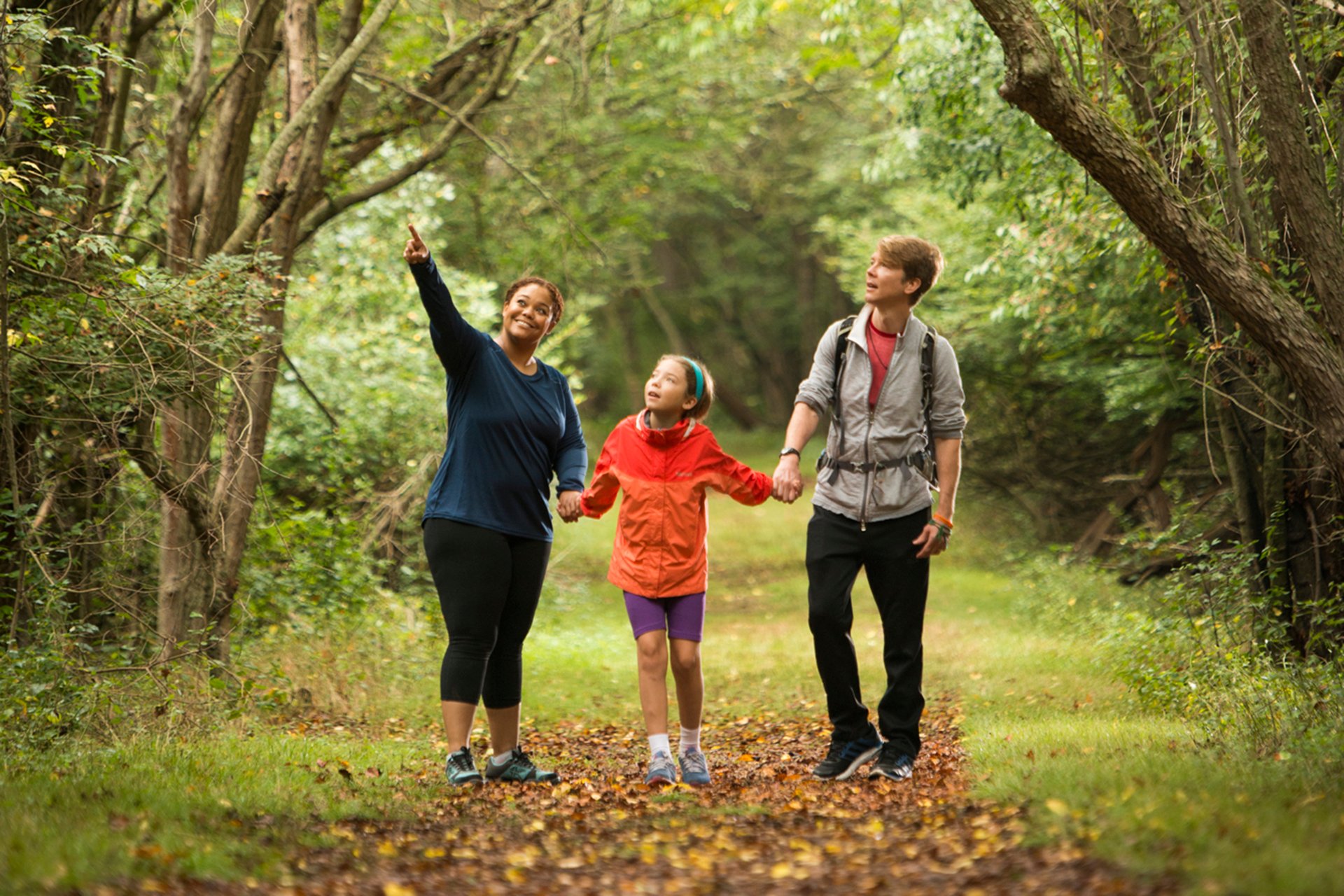 Parents holding hands with a child on a trail, mom pointing at something