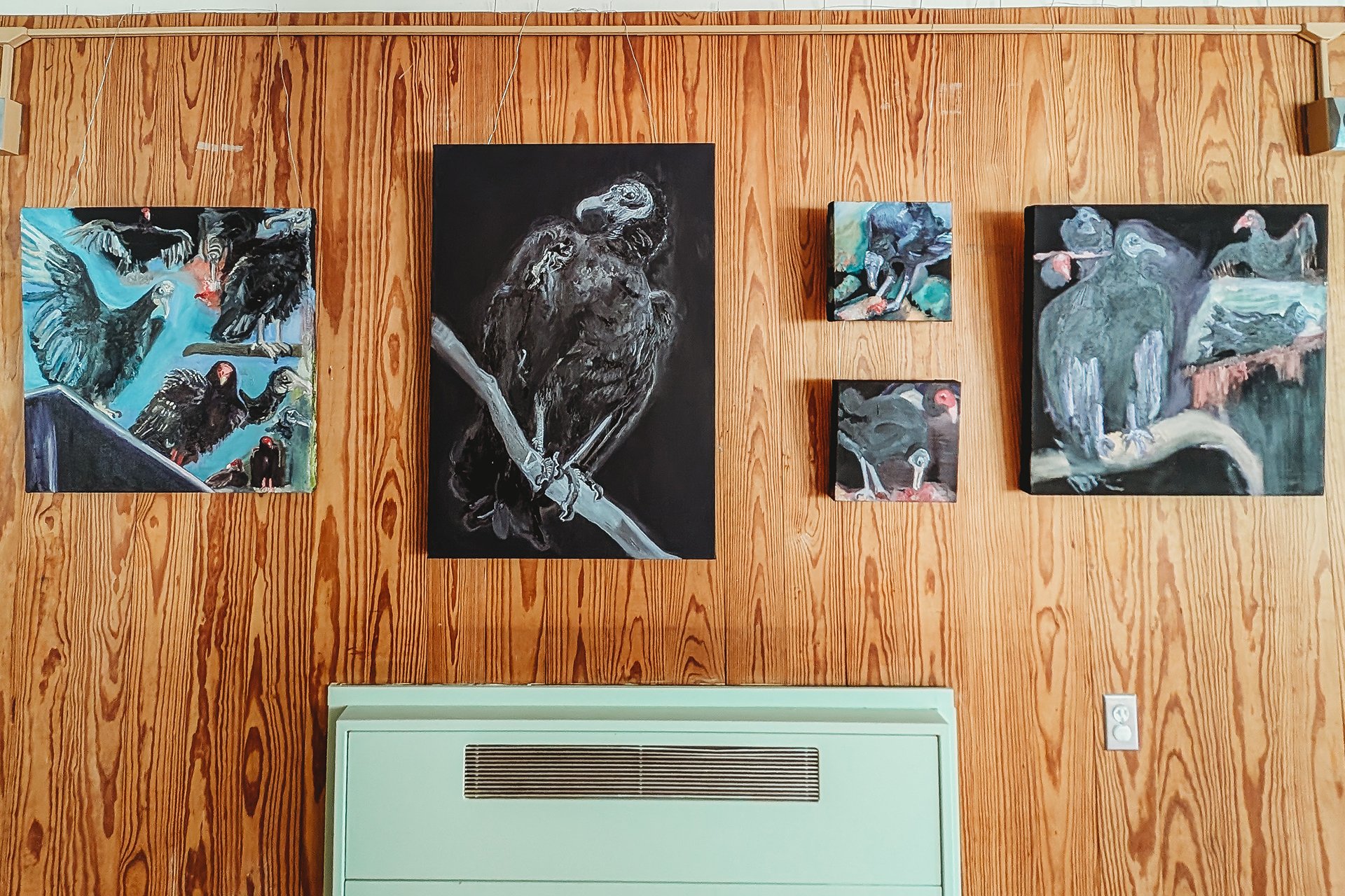 Five paintings of various sizes hung on a wood panel wall