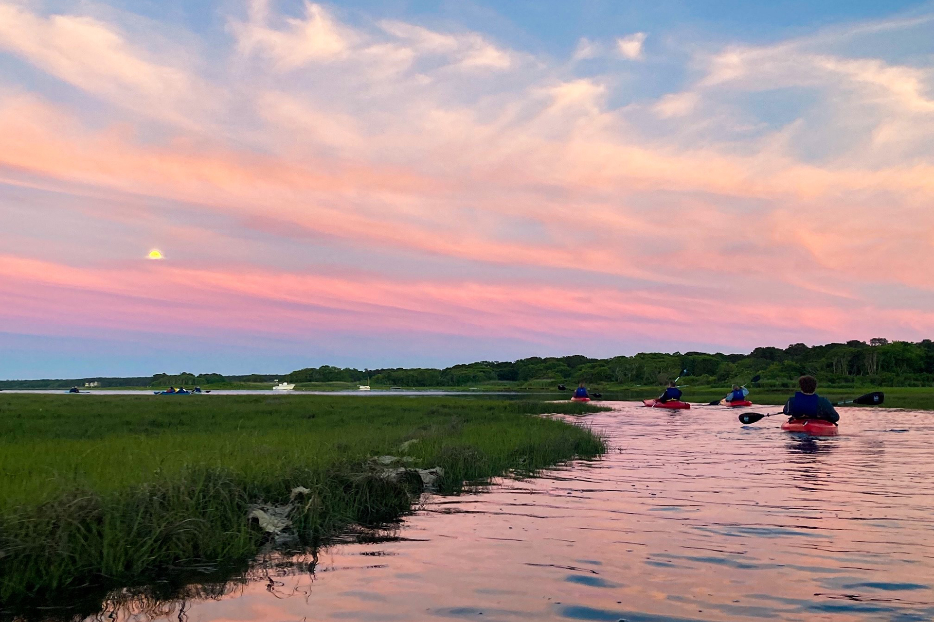 A small group kayaking through a marsh at sunset