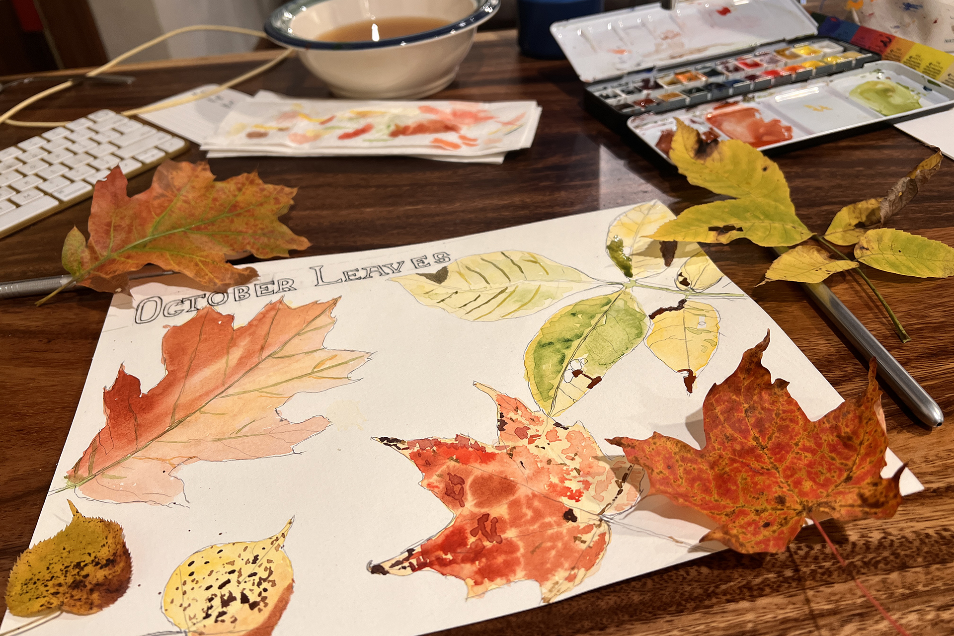 Piece of paper with watercolor of fall leaves on a table with art supplies
