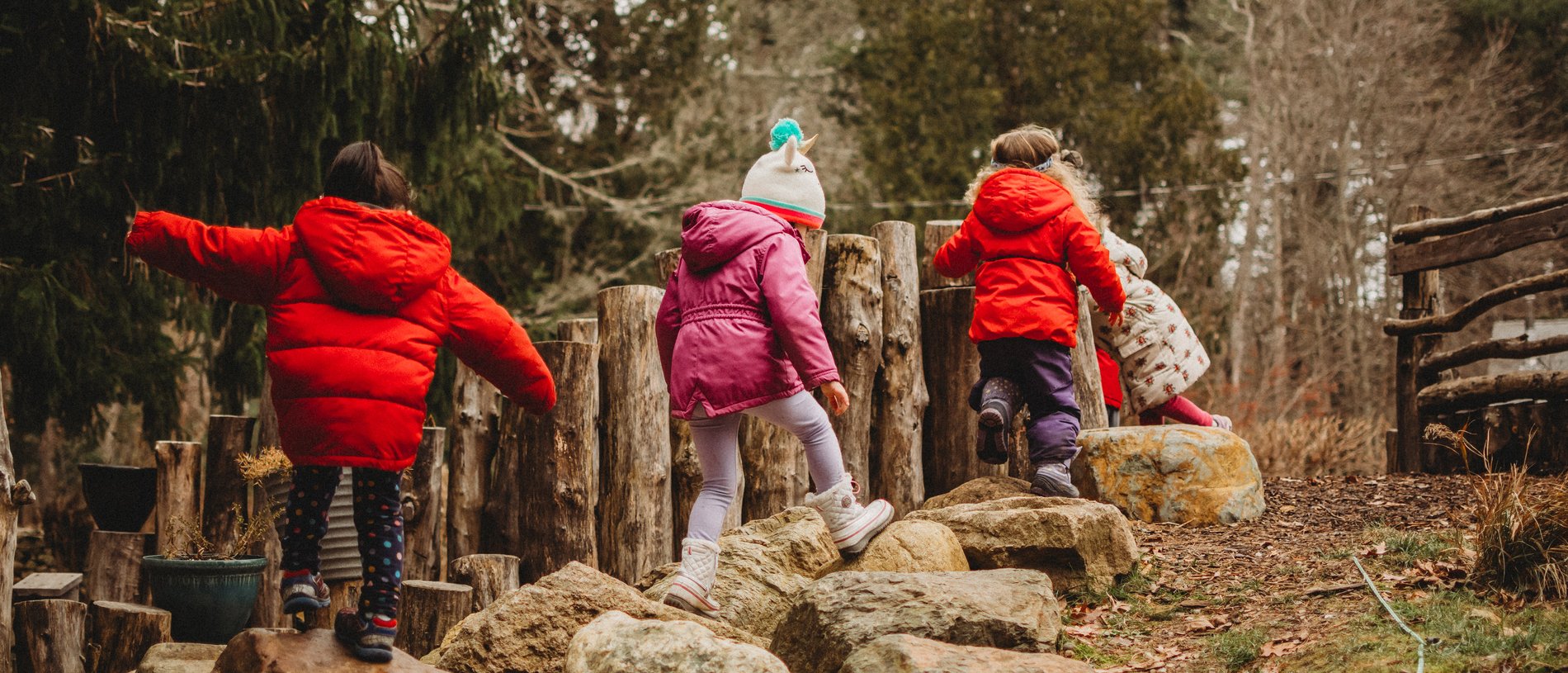 Kids in winter coats climbing rocks in a nature play area