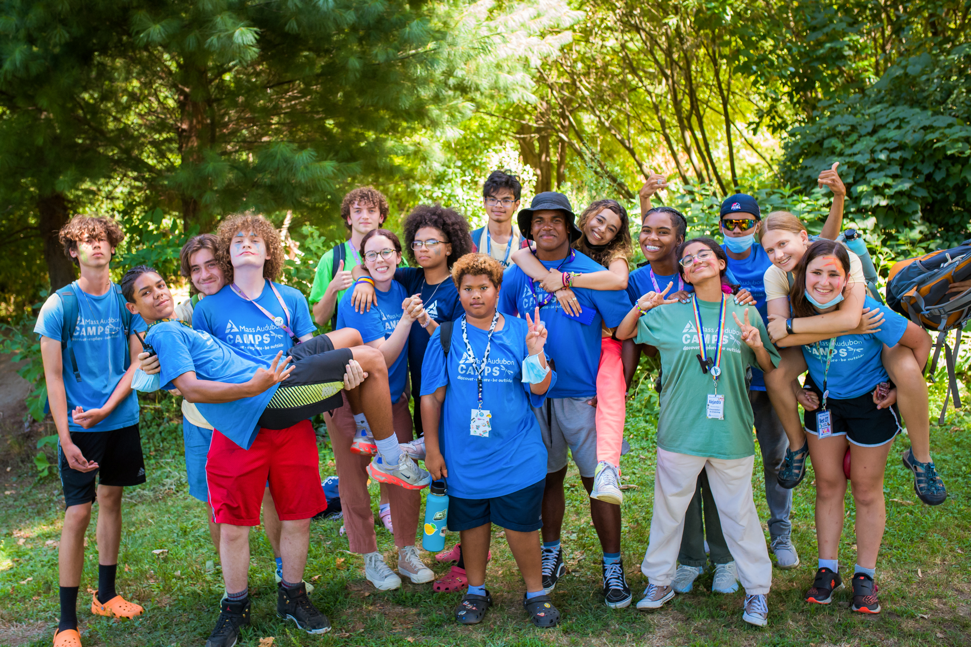 Counselors and CITs wearing blue and green Mass Audubon Camps staff shirts pose for a group photo