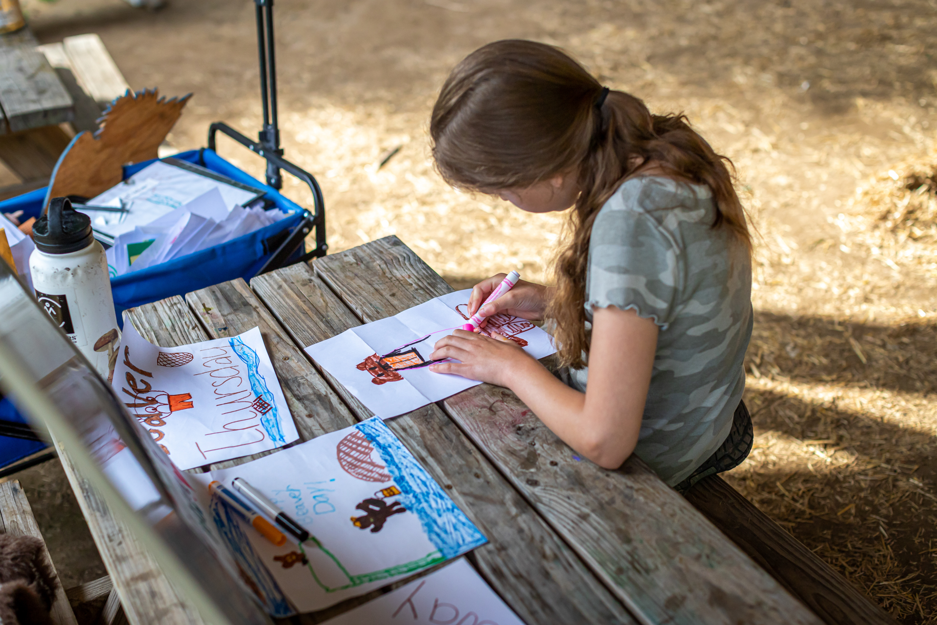 A camper at Arcadia Nature Camp sitting at a picnic table drawing pictures of wildlife with colorful markers