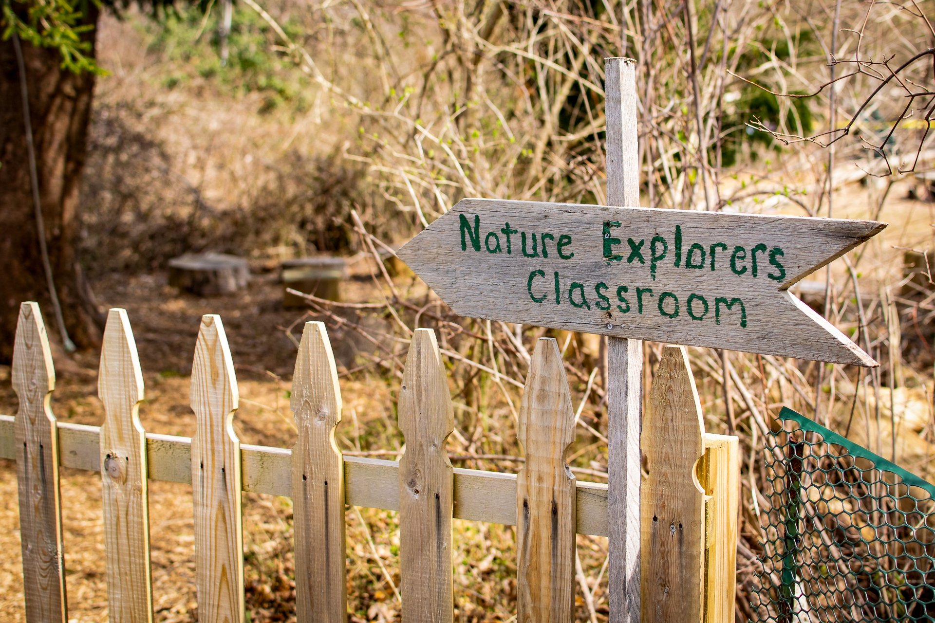 A wooden sign shaped like an arrow reads "Nature Explorers Classroom" and points to a Nature Play Area at Long Pasture Wildlife Sanctuary