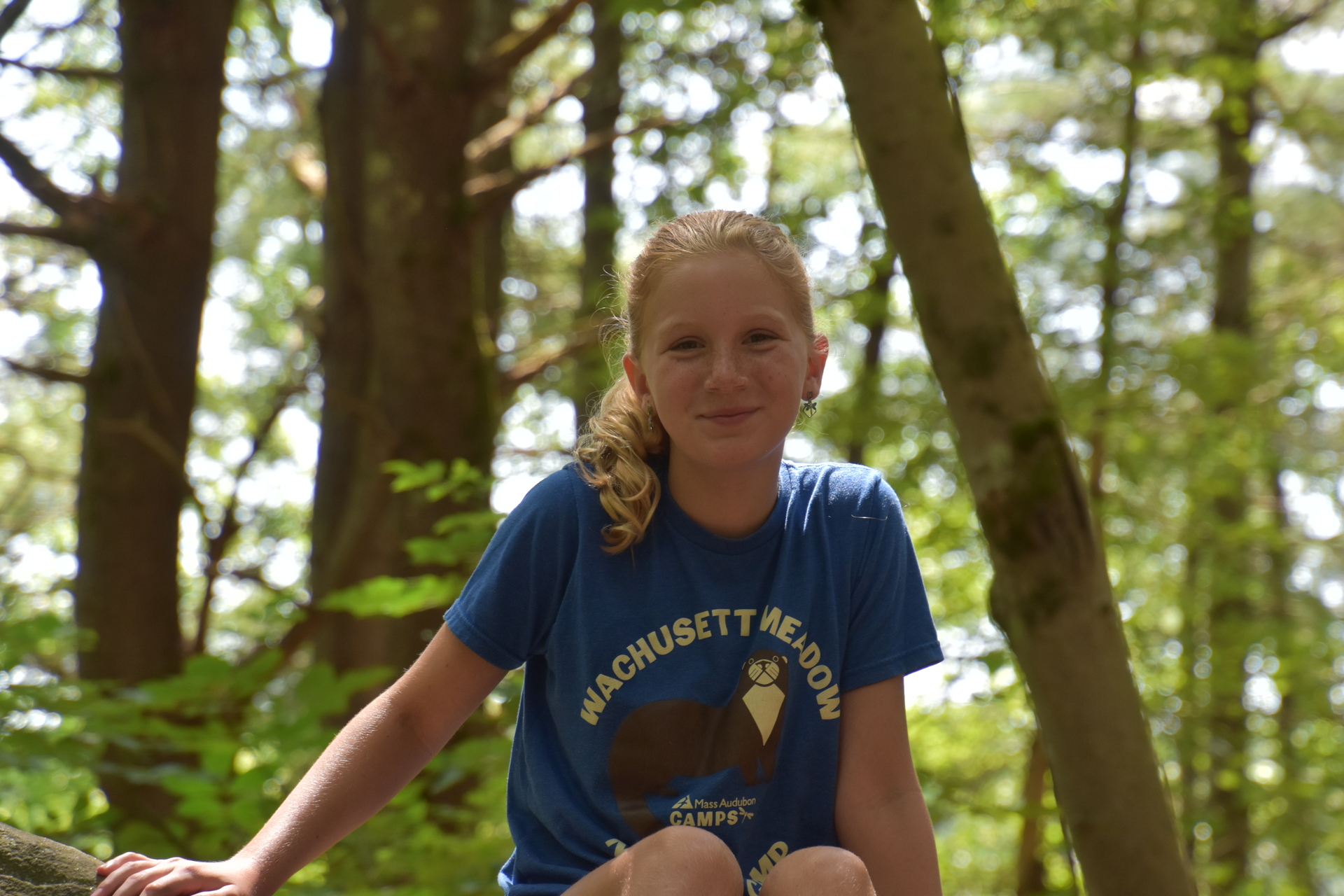 Camper sits on a log, smiling.