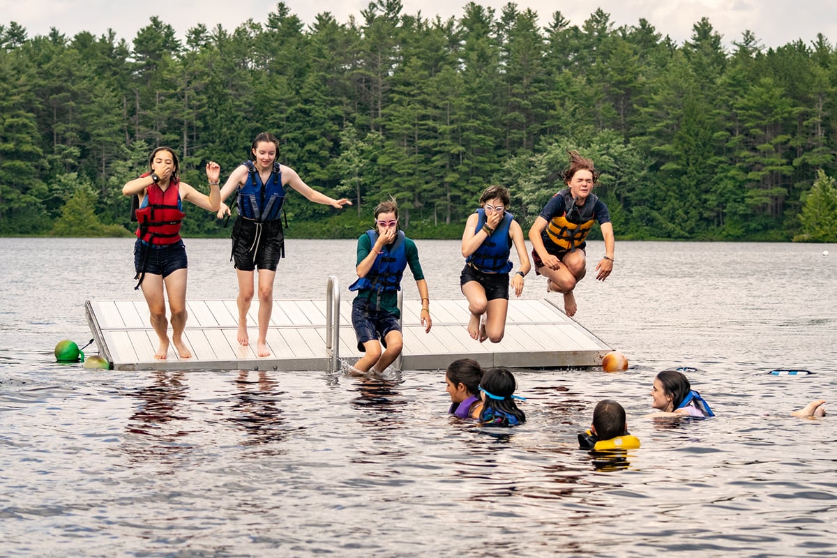 Campers jumping off a floating dock wearing life jackets.