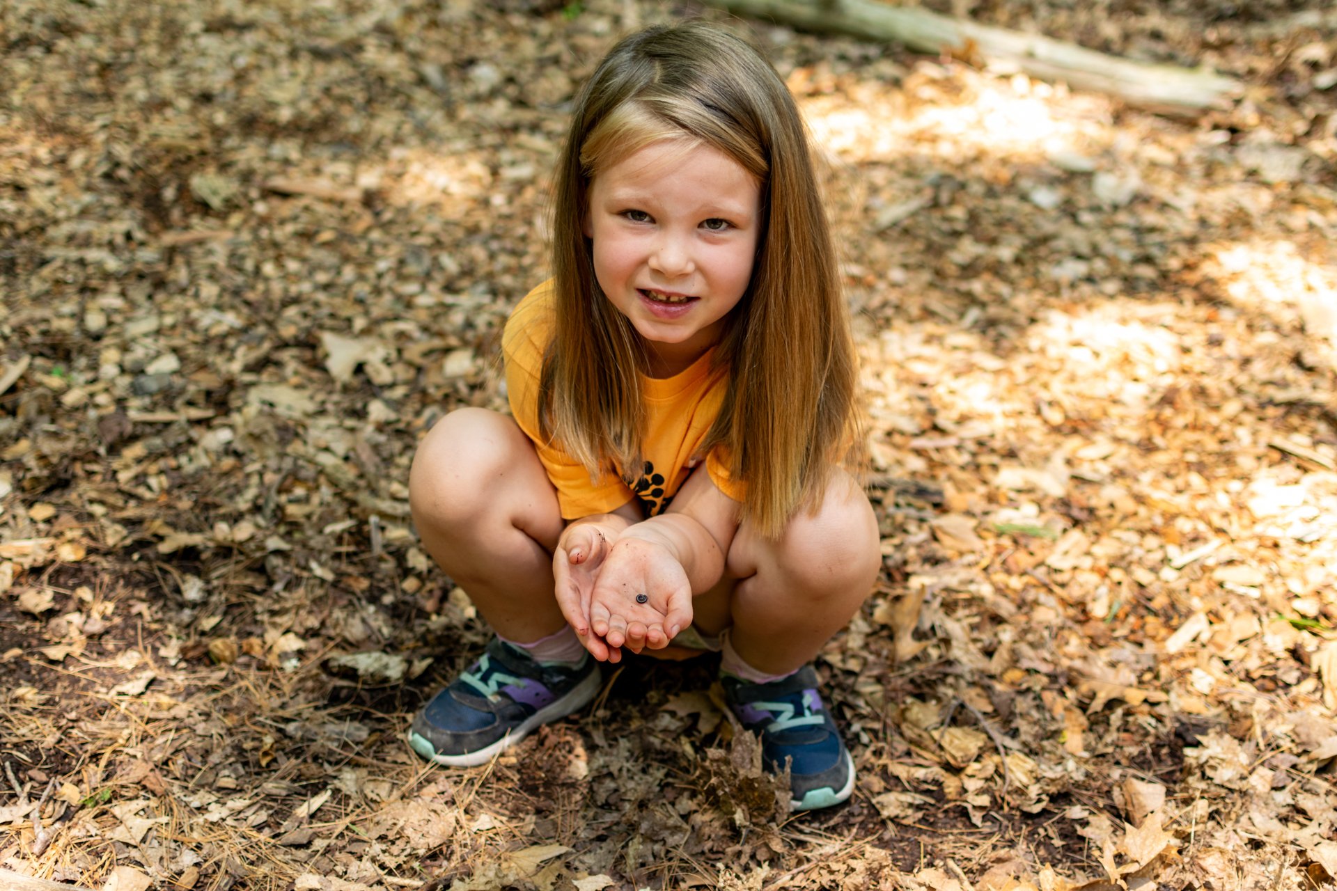 A camper at Habitat Nature Camp crouching and holding an insect in her hands