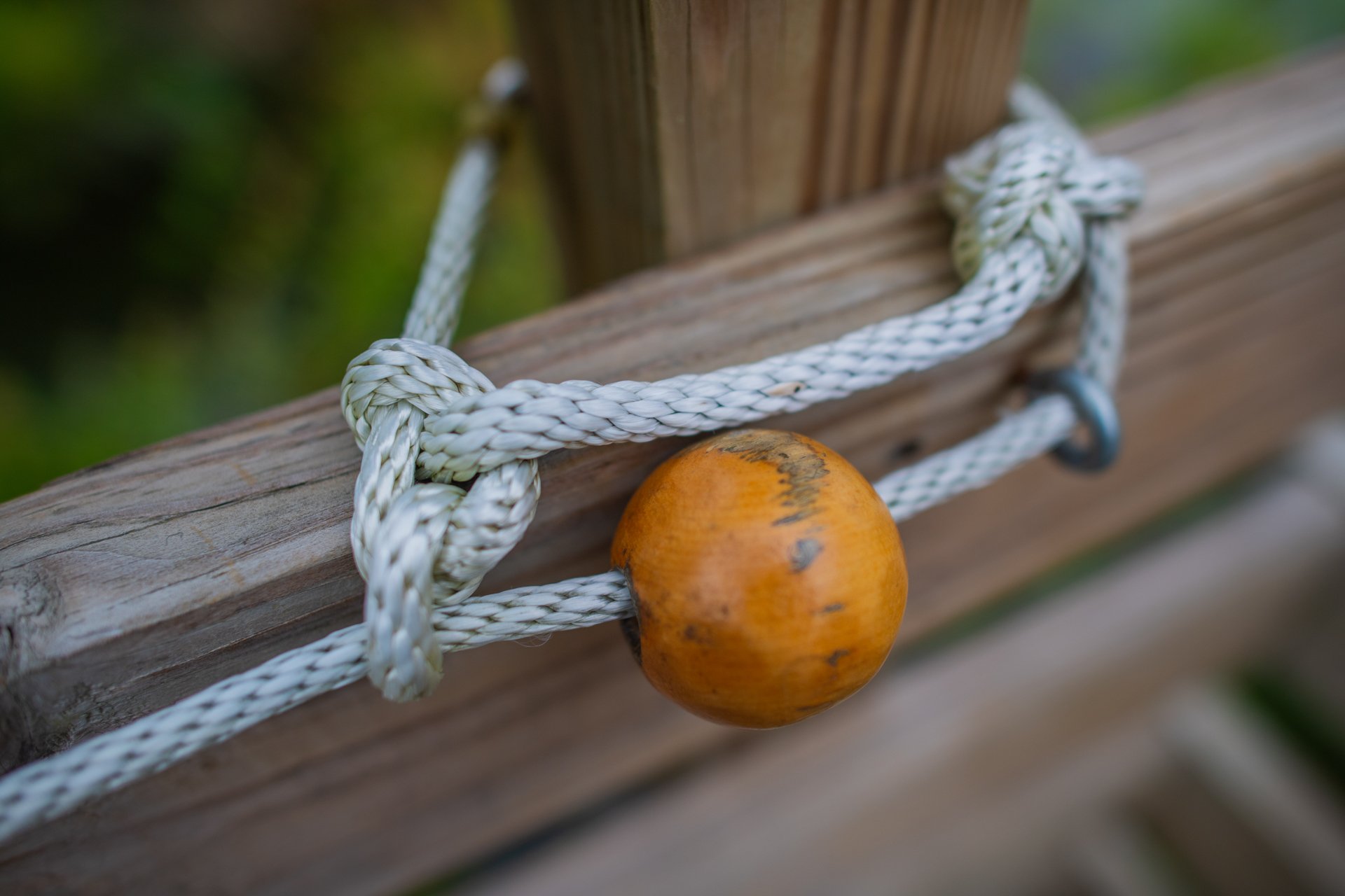 A close-up of a wooden bead on a rope tied around a wooden post, part of the tactile guidance system at Stony Brook's accessible All Persons Trail