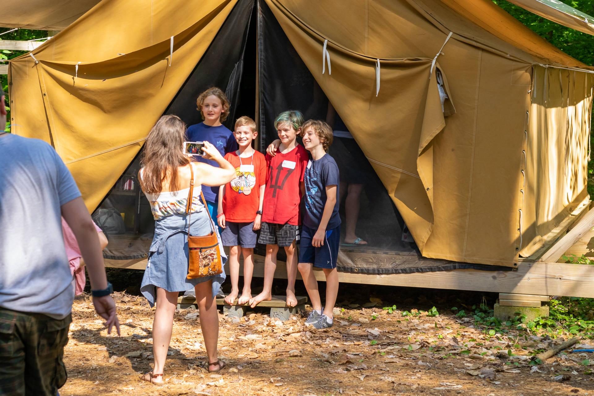 A group of four boys poses for a photo for a woman holding a smartphone in front of a yellow platform tent with the entrance flaps tied back.