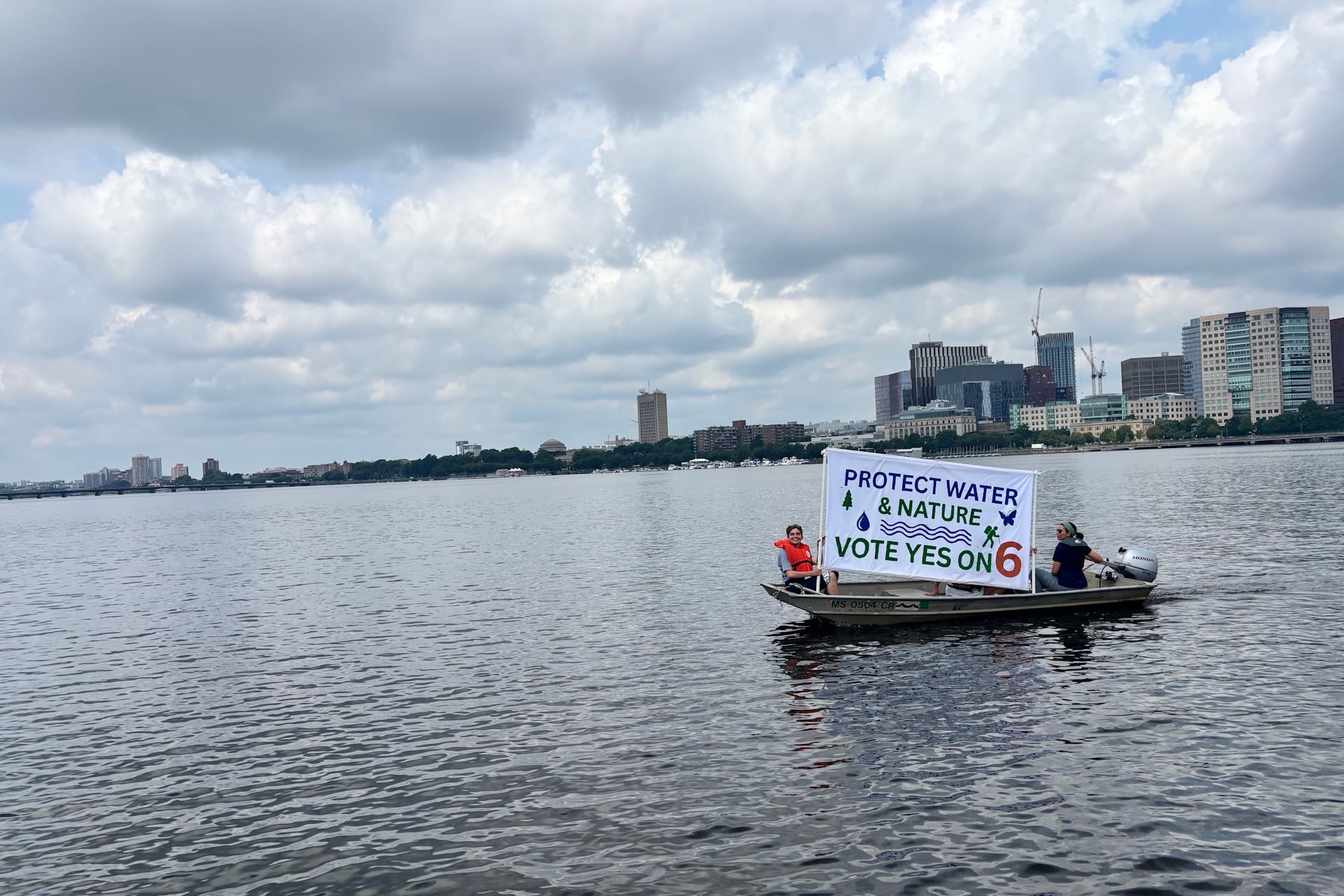 Two people with a banner that reads "Protect water and nature vote yes on 6" seen at a distance