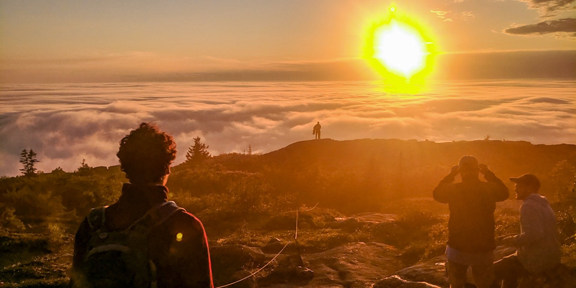 Wildwood teen trekker on a mountain summit, looking out across a sea of clouds below a golden sunset