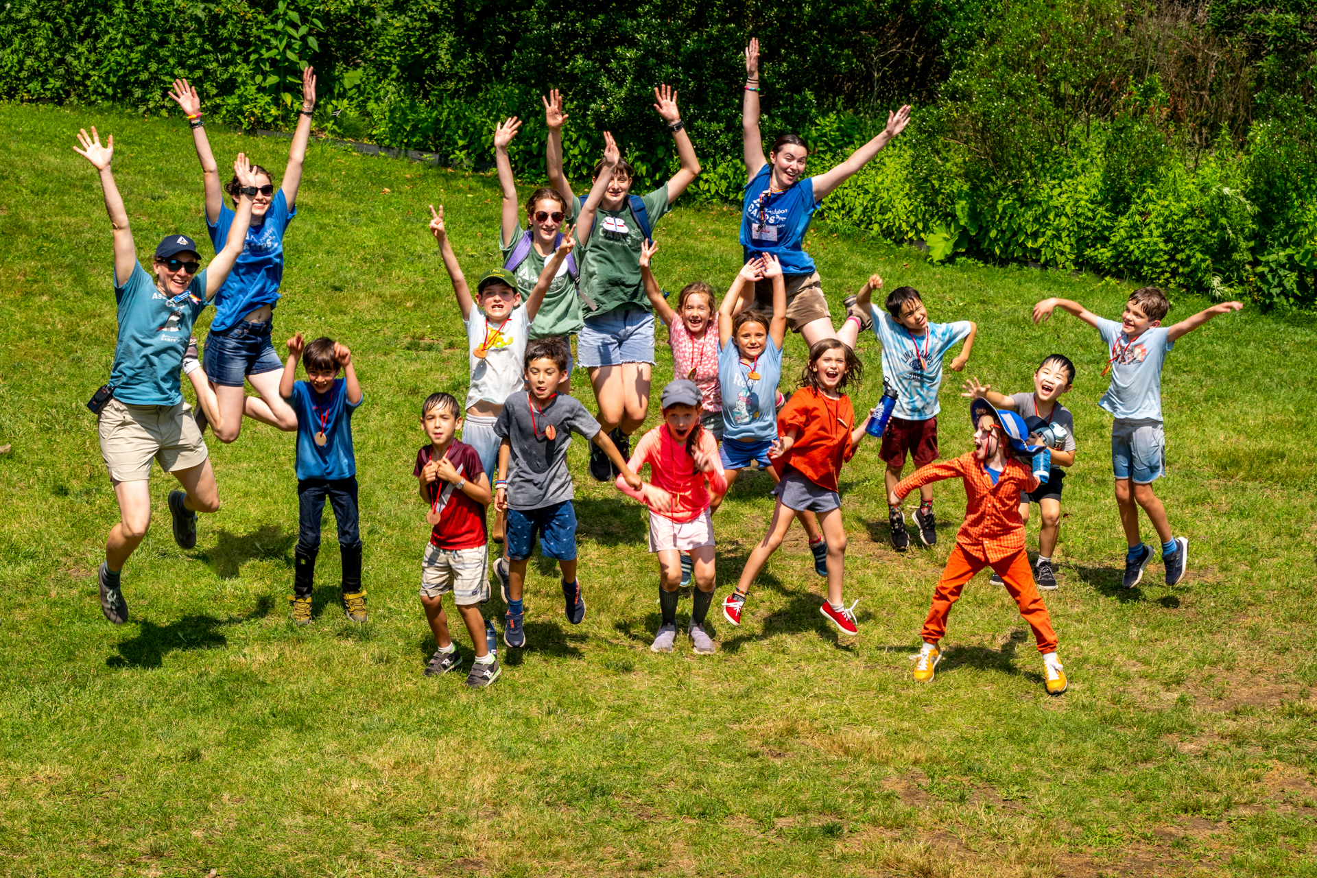 A group of smiling Broadmoor campers and counselors jumping into the air with their arms raised