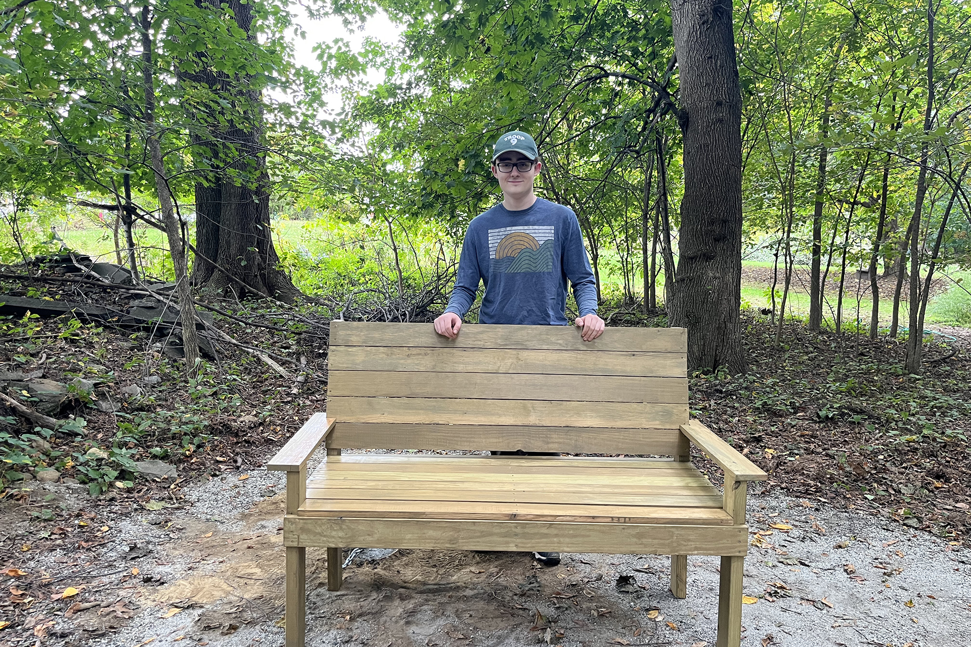Oliver Chase-Norris posing behind BMB's new bench on the All Persons Trail