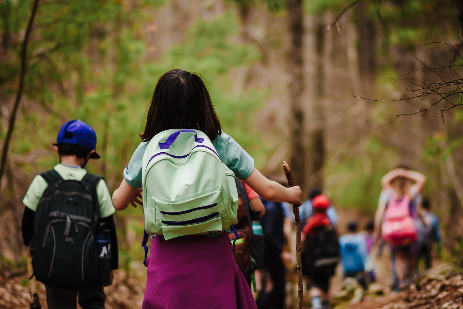Kids wearing backpacks walking away from the camera on a trail