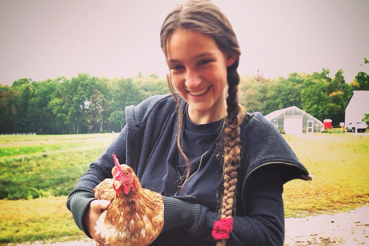 Girl with a long braid down her shoulder smiling and holding an orange and white chicken.