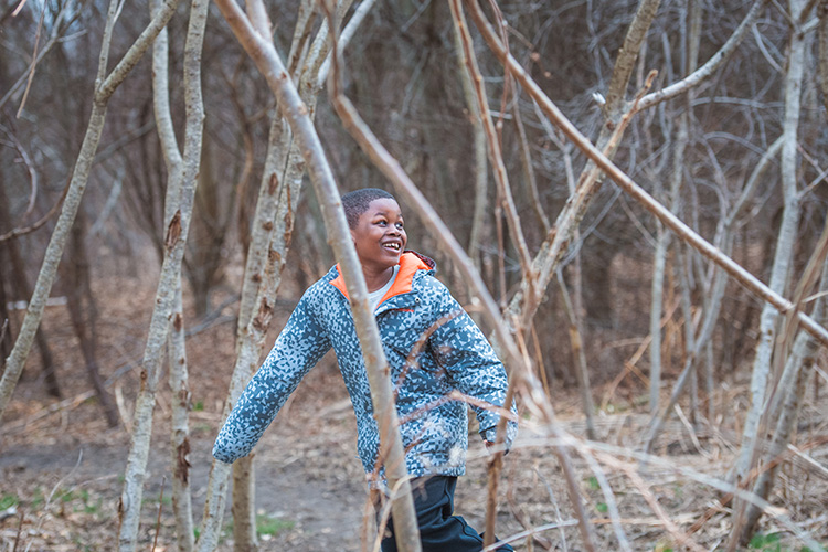 Young boy laughing while running through winter trees at Boston Nature Center